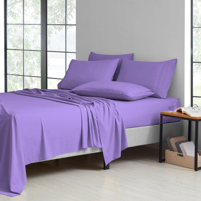 Purple bedding set on a bed in a room with large windows.