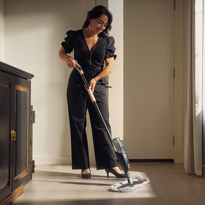 Woman cleaning a floor with a mop in a room with a window and furniture.
