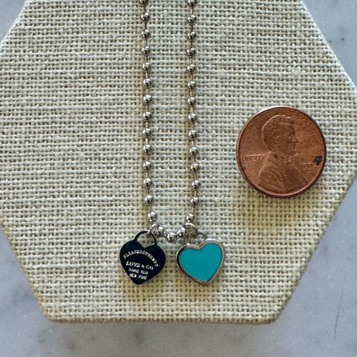 Necklace with heart-shaped charms on a hexagonal display card with a penny for scale.