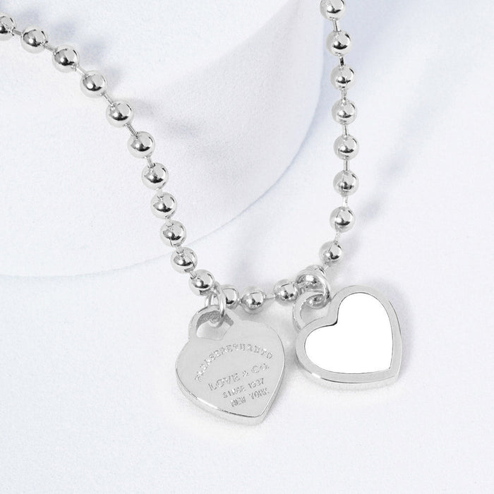A silver necklace featuring two heart-shaped charms on a ball chain.