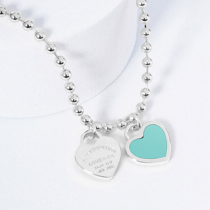 A silver necklace featuring two heart-shaped charms on a ball chain.