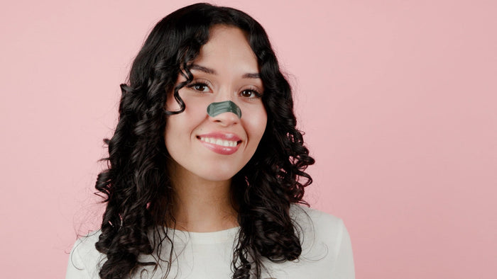 Woman with a green leaf on her nose against a pink background