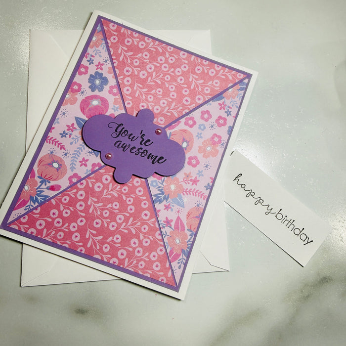 A handmade birthday card with a floral patterned envelope and a small white card reading 'happy birthday,' placed on a light marble-like surface.