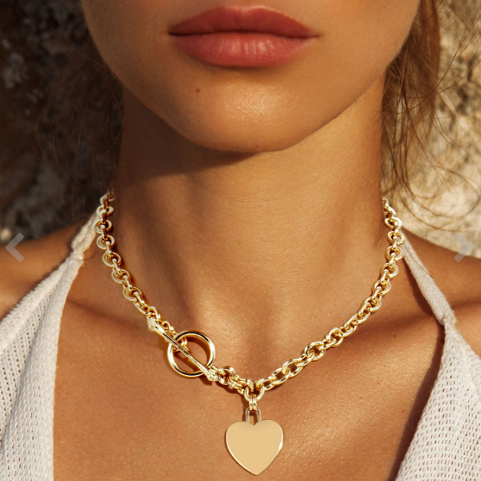 A close-up image of a woman wearing a gold toggle necklace with a heart pendant.
