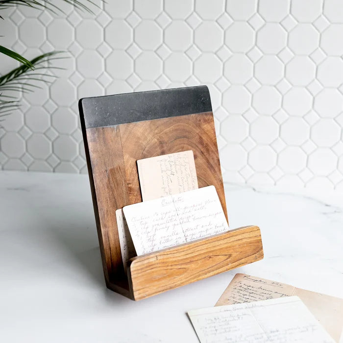 A cookbook holder made of mango wood with a solid black marble stone base, holding a cookbook and placed on a kitchen counter.