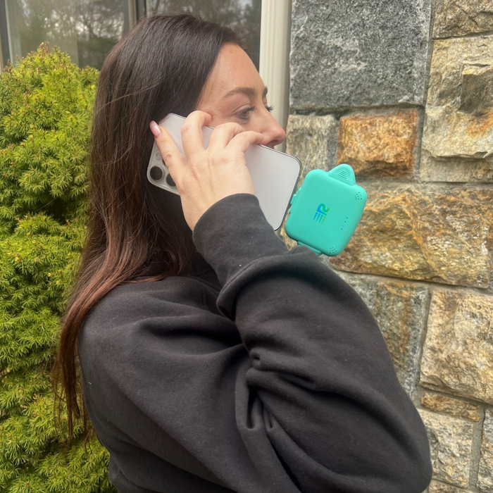 Person holding a phone with a teal case against a stone wall and greenery background