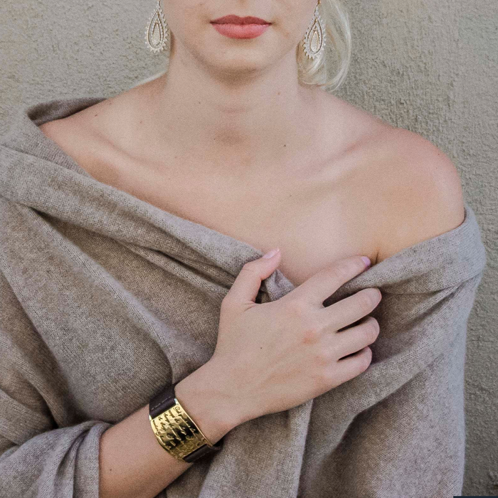 A person with a light complexion wearing a beige knit sweater and a gold-plated cuff bracelet with a serenity prayer inscription.